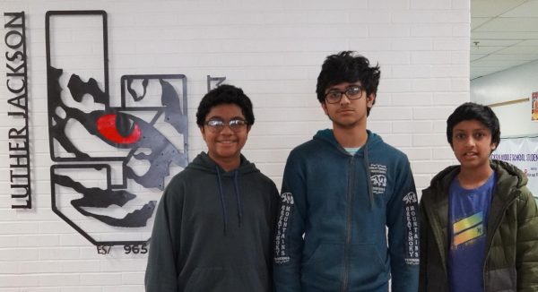 Bhavesh, Sir Pharoah, and Arnav standing in front of the Luther Jackson sign in the lobby.