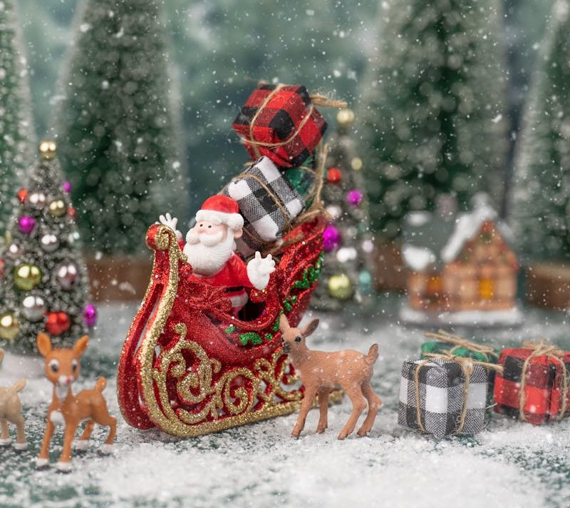 Miniature Santa sleigh amidst snow and decorated Christmas trees, evoking holiday cheer.